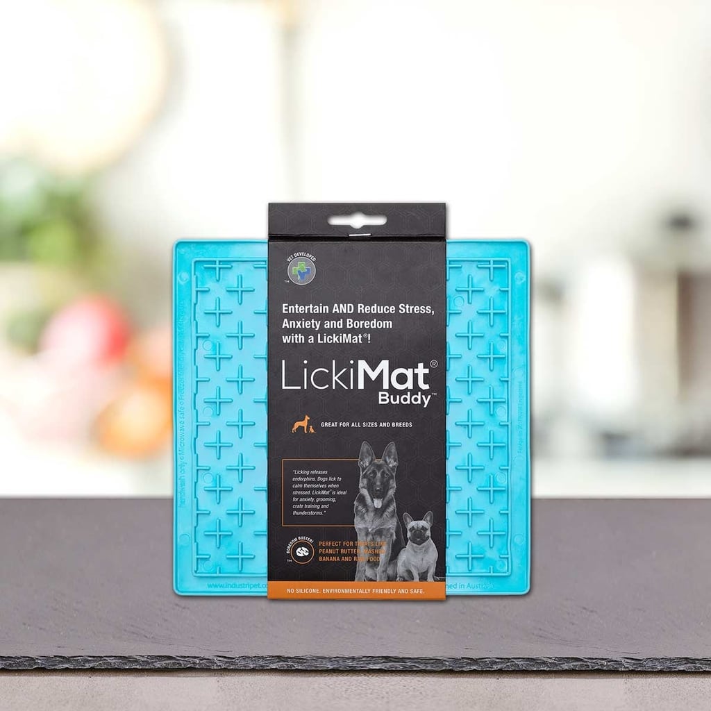 PLATINUM Podloga LickiMat® - BUDDY, prikazan v modri embalaži na pultu, pomaga zmanjšati stres, tesnobo in dolgčas pri psih in mačkah. Mehko zamegljeno ozadje poudarja izdelek.