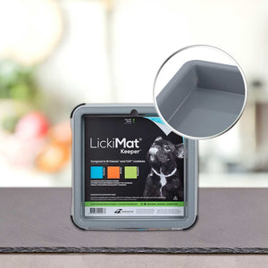 Siva PLATINUM LickiMat® - BUDDY KEEPER za hranjenje hišnih ljubljenčkov je razstavljena na pultu, z bližnjim posnetkom njenega vogala. Na etiketi izdelka je upodobljen pes in barvni deli besedila.