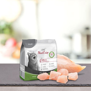 Vrečka PLATINUM MeatCrisp Adult Chicken, Suha Hrana za Mačke leži na sivi površini poleg surovih piščančjih prsi in koščkov. Na embalaži je upodobljena srečna mačka in poudarjen postopek Freshmeatdryer za odrasle mačke z okusom piščanca.