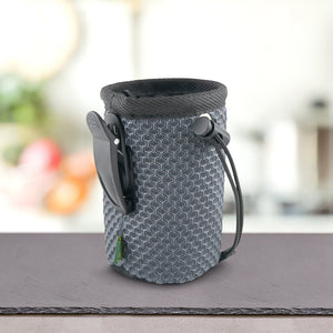 Siva, teksturirana, valjasta torbica z vrvico in plastično sponko za pas, idealna za prenašanje PLATINUM Paket okusov Priboljškov za Pse, je postavljena na pult z zamegljenim kuhinjskim ozadjem.